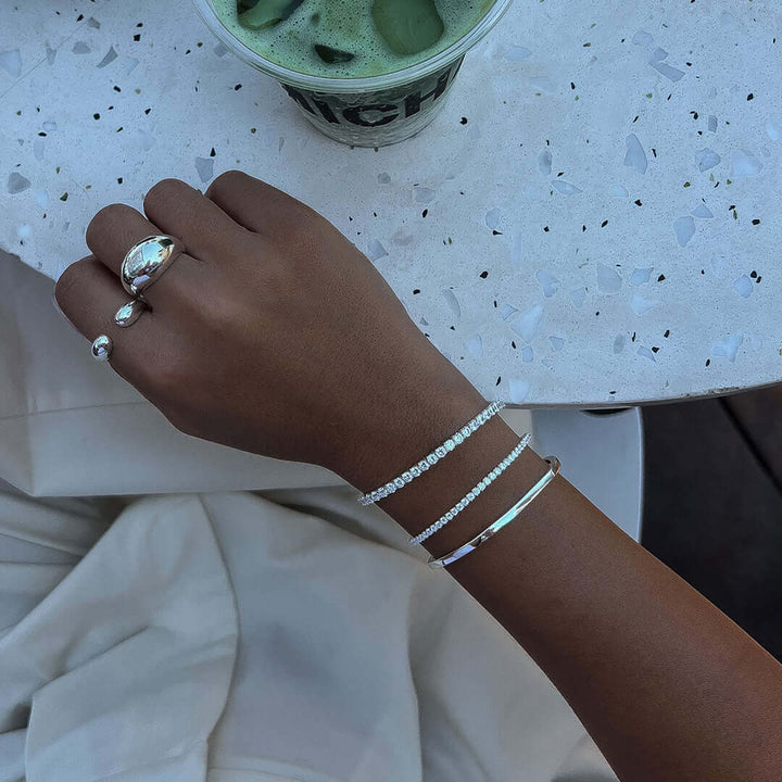 Elegant hand wearing the Alice Tennis Bracelet alongside silver rings, perfect for stylish stacking.