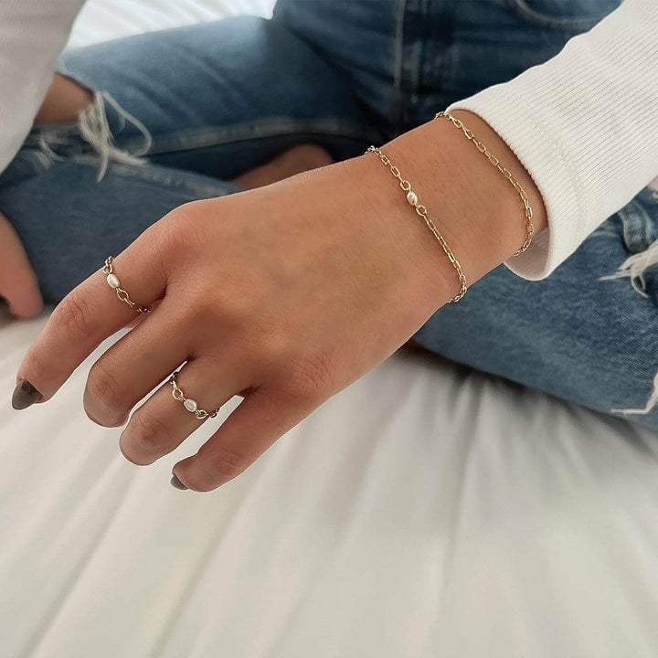 A close-up of a hand wearing a Poly Ring alongside delicate bracelets in a chic outfit.