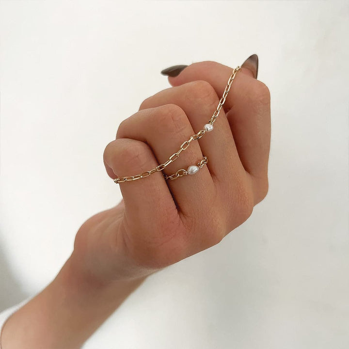 A hand wearing the Poly Ring with a delicate chain design and a freshwater pearl, showcasing a chic minimal vibe.