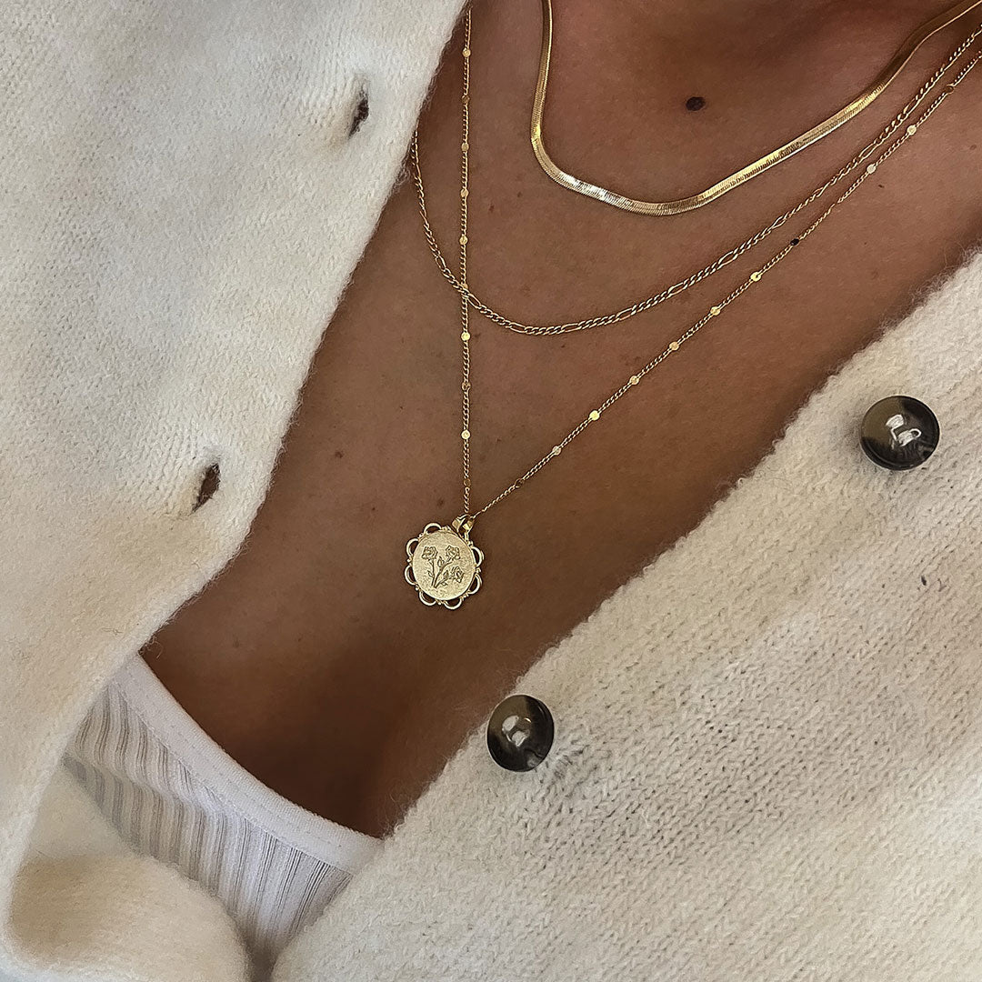 Close-up of a woman wearing a Lace Necklace with a floral pendant layered with other delicate gold chains.