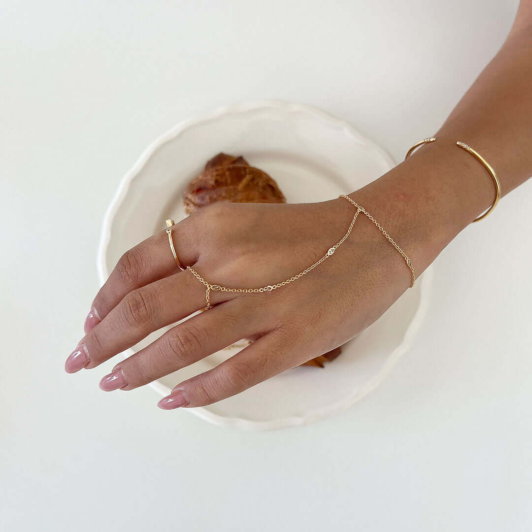 Sol Hand Chain Bracelet worn on a hand with a croissant in the background, showcasing its chic design and sparkling crystal.