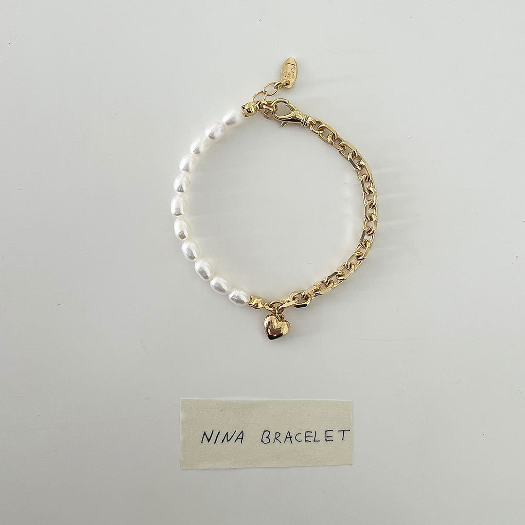 Nina Bracelet featuring a delicate chain, natural pearls, and a bold heart charm for a stylish look.