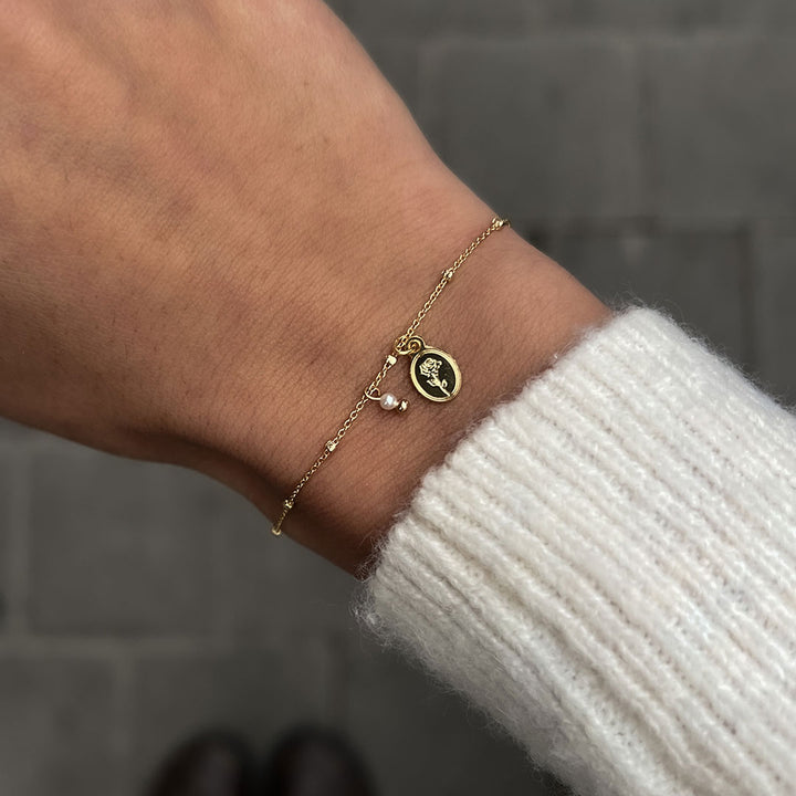 Flory Bracelet worn on wrist featuring delicate chain, oval charm with rose, and natural pearl detail.