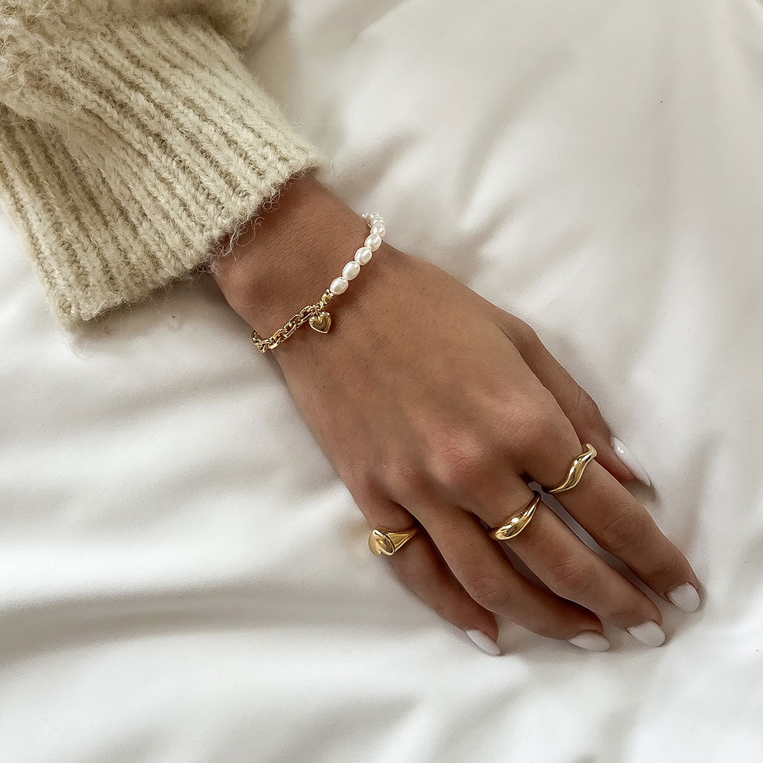 Nina Bracelet featuring natural pearls and a heart charm, styled on a hand with gold rings and a knitted sweater.