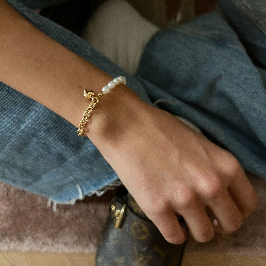 Nina Bracelet featuring a delicate chain, natural pearls, and a bold heart charm, worn on a wrist.