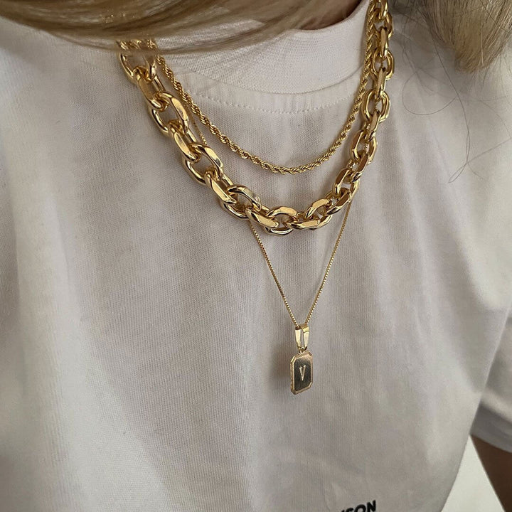 Dylan Necklace Set featuring layered gold chains and an initial pendant on a model in a casual white t-shirt.