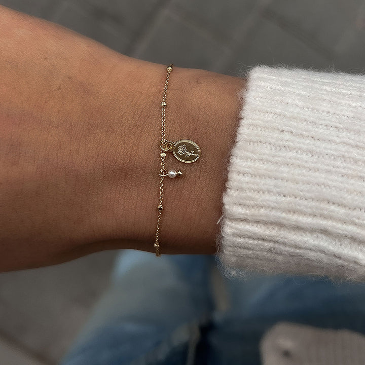 Flory Bracelet featuring a delicate chain, oval charm with rose, and natural pearl, worn elegantly on a wrist.