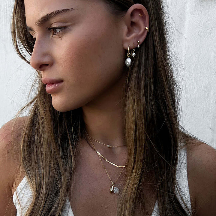 Model showcasing May Earrings featuring delicate hoop and freshwater pearl, styled with layered necklaces.