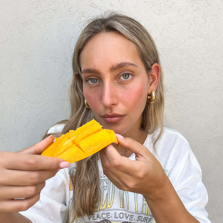 Model wearing Mango Earrings, holding a slice of ripe mango, showcasing summer fashion and fruit inspiration.
