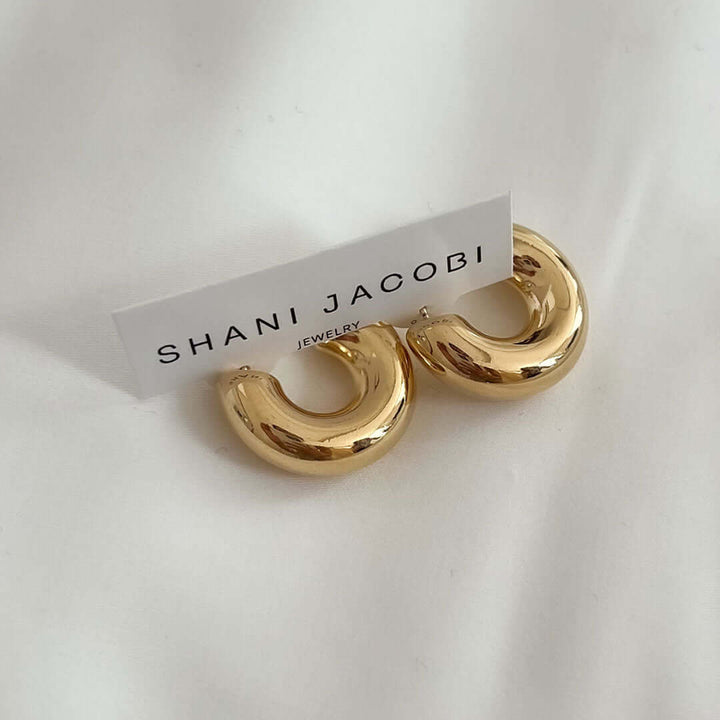 Golden hoop Mango Earrings from Shani Jacobi Jewelry displayed on soft fabric.
