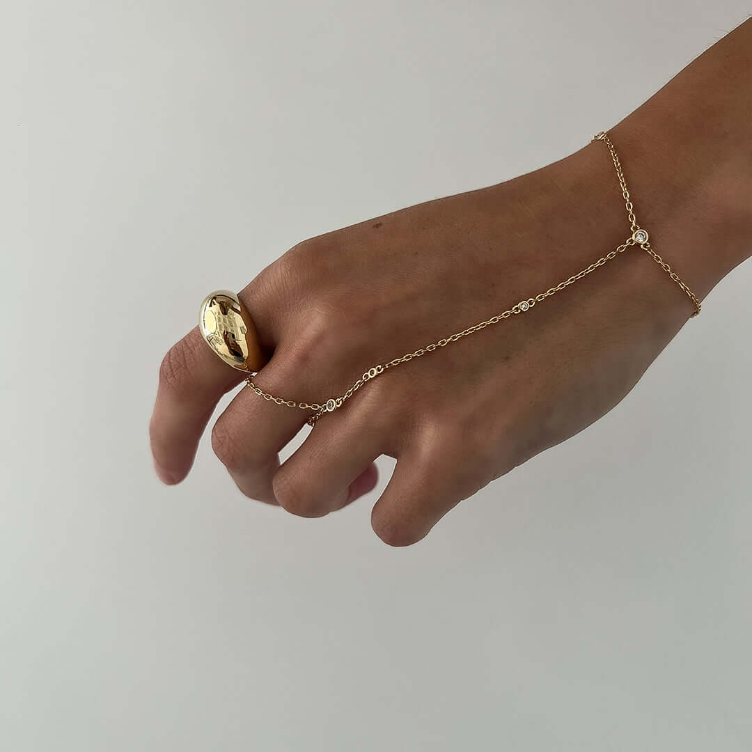 A hand wearing a bold Olive Ring featuring a teardrop design and gold chain, showcasing its stylish appeal.