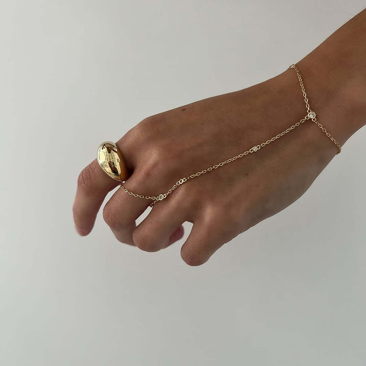 A hand wearing a bold Olive Ring featuring a teardrop design and gold chain, showcasing its stylish appeal.