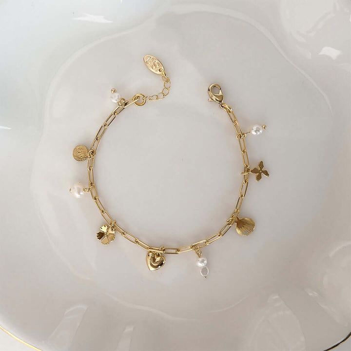 Dainty gold chain bracelet by Shani Jacobi with pearls and playful charms like hearts, clovers, and seashells.