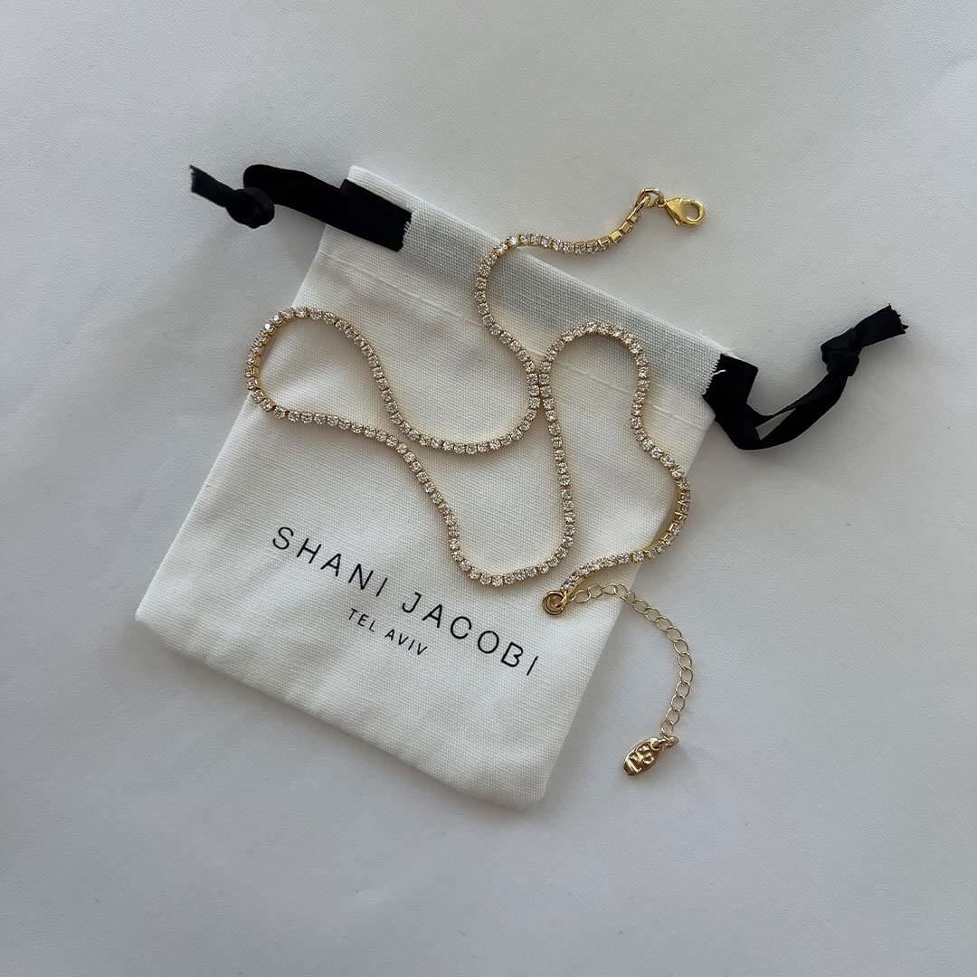 Tennis necklace by Shani Jacobi in a drawstring pouch, featuring 14K gold plated brass and crystal stones.