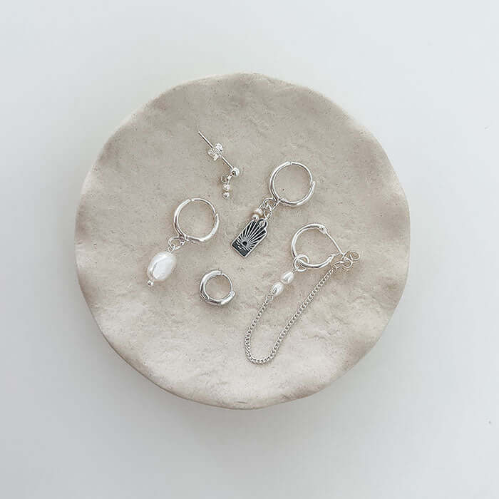 Sunset Earrings Set displayed on a soft round dish, featuring an engraved sunset charm and unique designs.